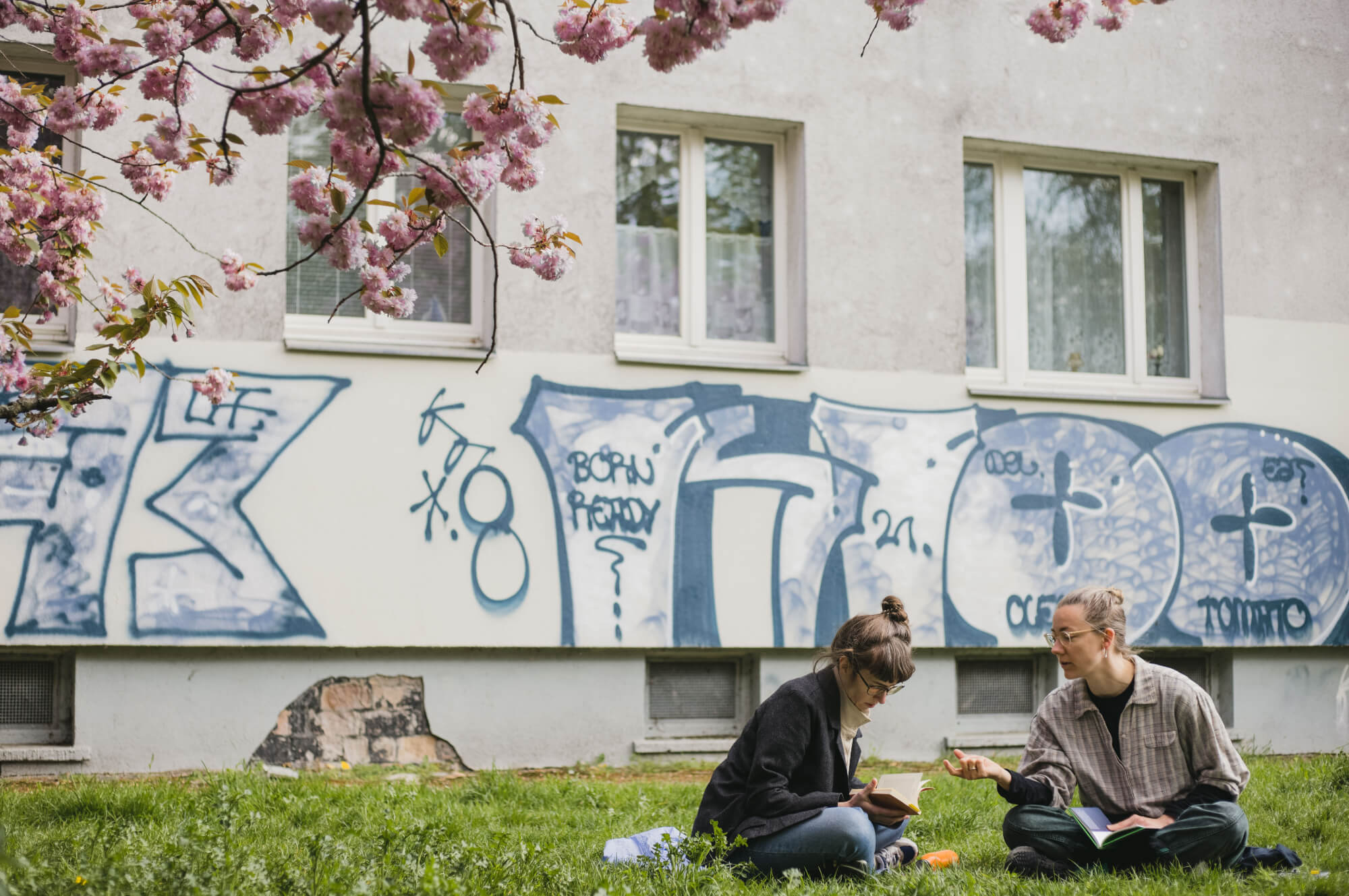 Ricarda und Kathrin lesend und sprechend auf einer Wiese sitzend